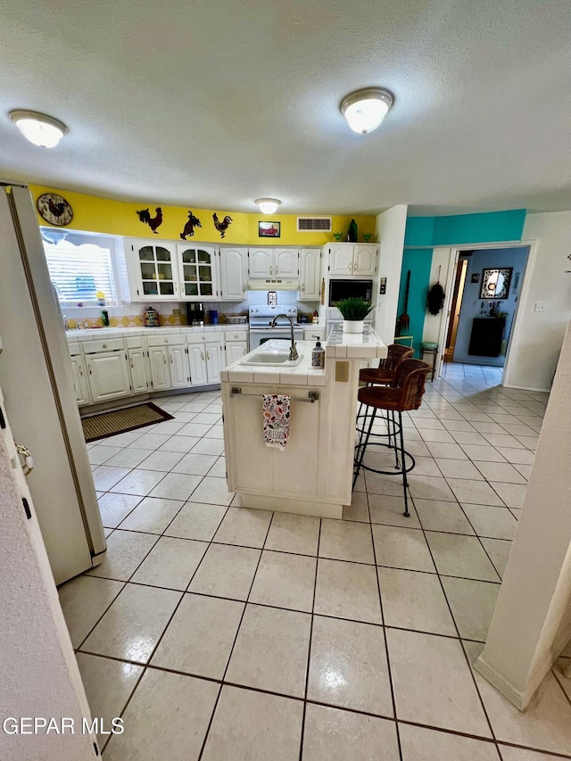 16899 Old Butterfield Trl, El Paso, TX 79938 - kitchen with tile countertops, a textured ceiling, light tile patterned floors, white cabinetry, and a kitchen island with sink