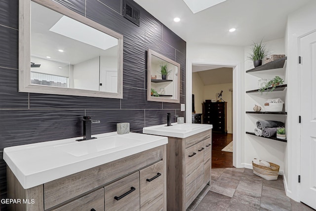 840 Tepic Dr, El Paso, TX 79912 - full bathroom featuring a skylight, two vanities, backsplash, stone finish flooring, and baseboards