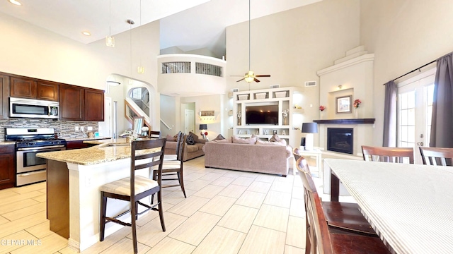 5712 Valley Lilac Ln, El Paso, TX 79932 - kitchen featuring stainless steel appliances, a breakfast bar, a towering ceiling, a ceiling fan, and a glass covered fireplace