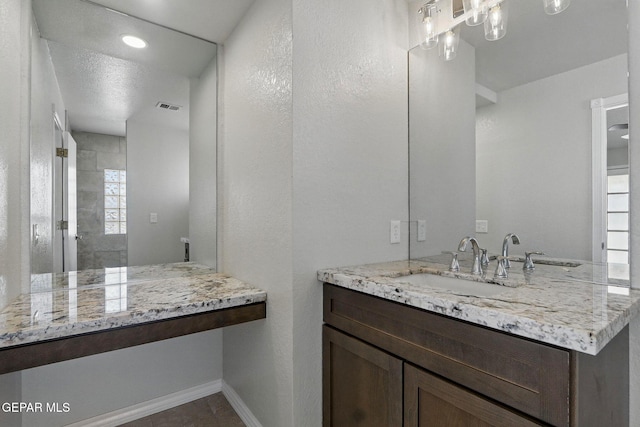 1718 Dean Jones Dr, El Paso, TX 79936 - bathroom with baseboards, a tile shower, vanity, and a textured wall