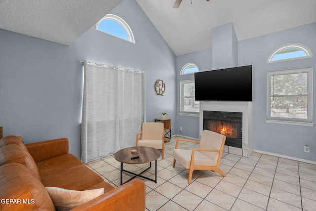 1640 Dennis Babjack Dr, El Paso, TX 79936 - living room with high vaulted ceiling, a lit fireplace, a ceiling fan, light tile patterned floors, and baseboards