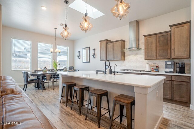 13436 Emerald Crystal Dr, El Paso, TX 79928 - kitchen with a chandelier, wall chimney range hood, a skylight, a kitchen island with sink, and light countertops