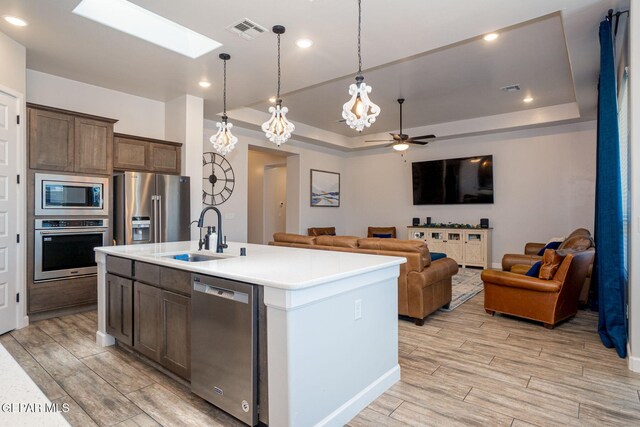 13436 Emerald Crystal Dr, El Paso, TX 79928 - kitchen with stainless steel appliances, a sink, a tray ceiling, a ceiling fan, and light wood-style flooring