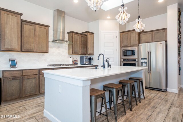 13436 Emerald Crystal Dr, El Paso, TX 79928 - kitchen featuring stainless steel appliances, wall chimney exhaust hood, a sink, a chandelier, and a kitchen island with sink