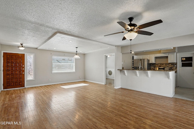 10224 Galahad Way, El Paso, TX 79924 - unfurnished living room featuring a textured ceiling, ceiling fan, light wood-style flooring, and baseboards