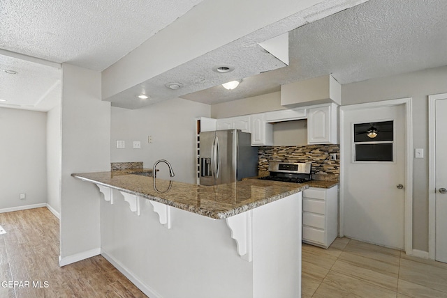 10224 Galahad Way, El Paso, TX 79924 - kitchen featuring appliances with stainless steel finishes, a kitchen breakfast bar, dark stone countertops, a textured ceiling, and tasteful backsplash