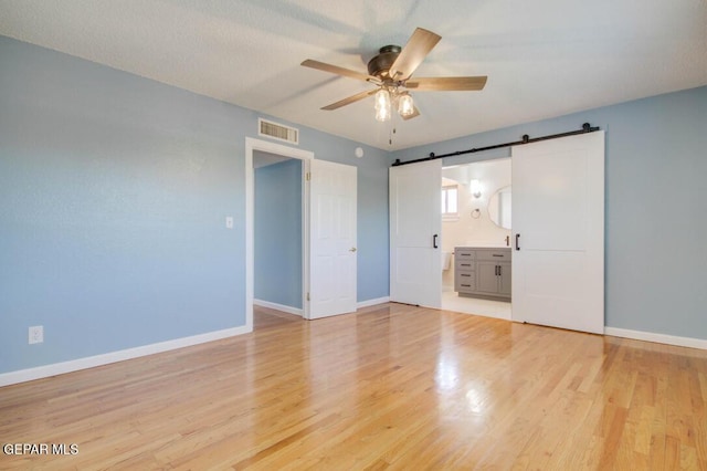 1701 Paul Moran Pl, El Paso, TX 79936 - unfurnished bedroom with a barn door, light wood finished floors, baseboards, and ensuite bathroom