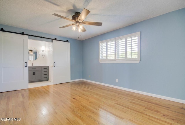1701 Paul Moran Pl, El Paso, TX 79936 - unfurnished bedroom with a barn door, light wood finished floors, baseboards, and a textured ceiling
