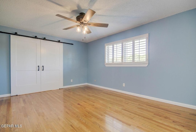 1701 Paul Moran Pl, El Paso, TX 79936 - unfurnished bedroom featuring a barn door, light wood-style flooring, baseboards, a textured ceiling, and ceiling fan