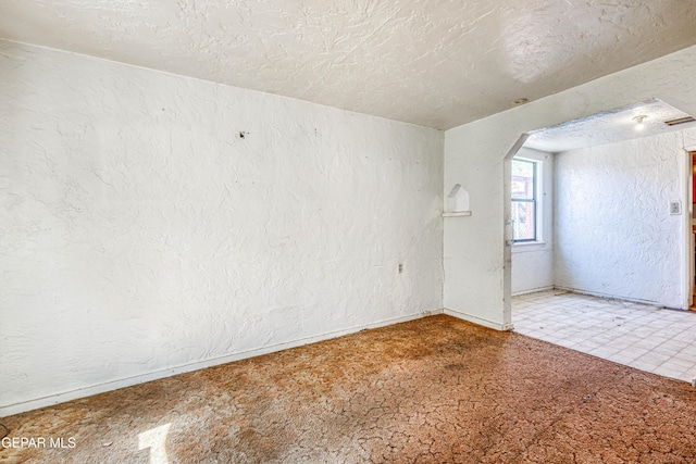 124 N Toledo Pl, El Paso, TX 79905 - empty room with a textured wall, baseboards, arched walkways, and a textured ceiling