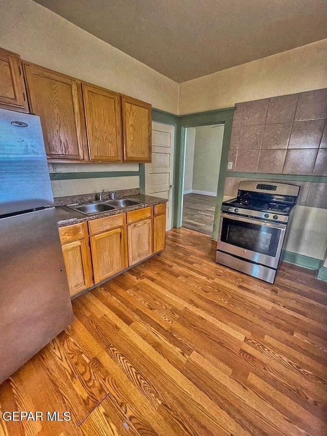 2526 Yandell Dr, El Paso, TX 79903 - kitchen featuring stainless steel appliances, a sink, light wood finished floors, dark countertops, and brown cabinetry