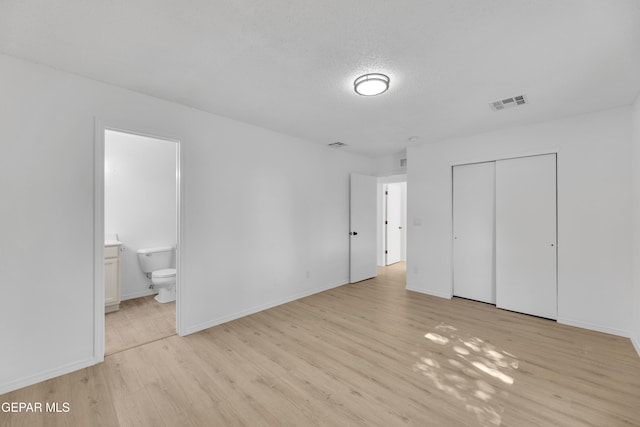11590 Flor Liatris Dr, Socorro, TX 79927 - unfurnished bedroom with light wood finished floors, a closet, baseboards, ensuite bath, and a textured ceiling
