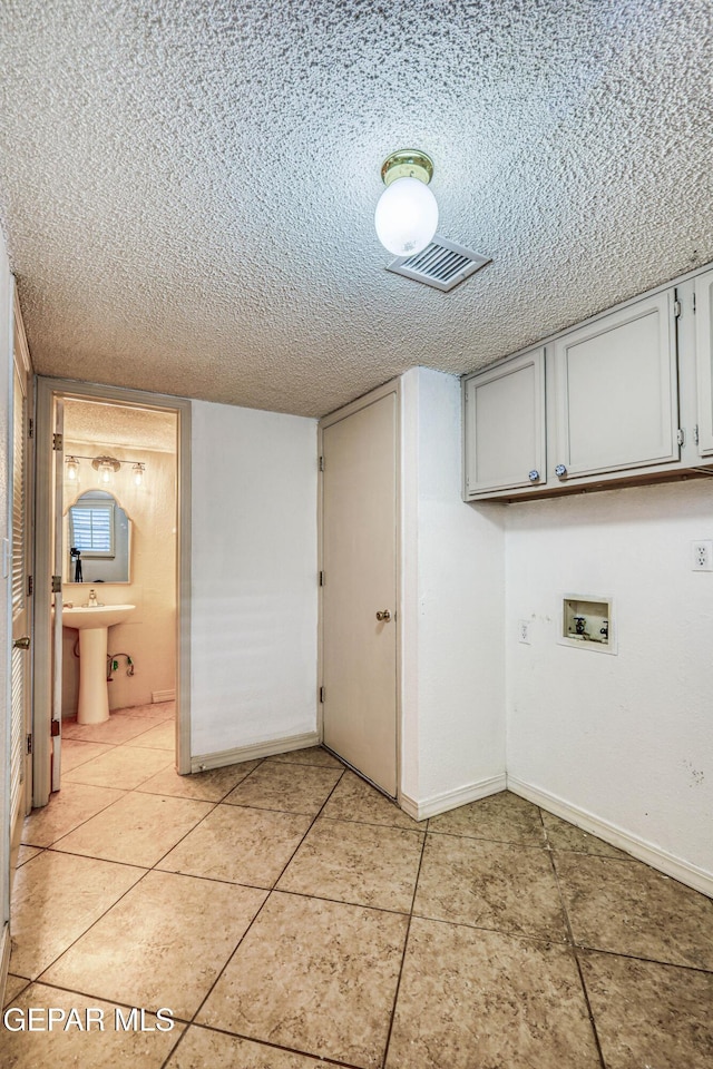 11513 Cree Ct, El Paso, TX 79936 - laundry room featuring hookup for a washing machine, cabinet space, a textured ceiling, baseboards, and light tile patterned floors