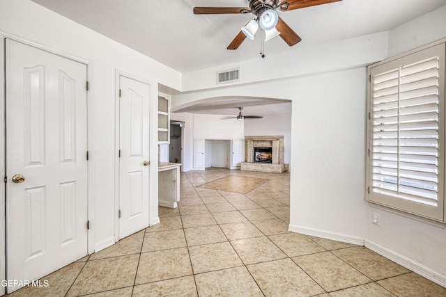 11513 Cree Ct, El Paso, TX 79936 - unfurnished living room featuring ceiling fan, light tile patterned floors, a fireplace with raised hearth, arched walkways, and baseboards