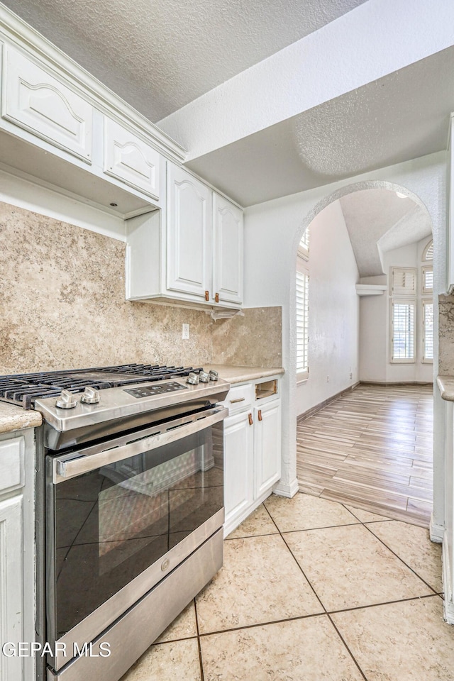 11513 Cree Ct, El Paso, TX 79936 - kitchen with stainless steel gas range, tasteful backsplash, light countertops, arched walkways, and white cabinetry
