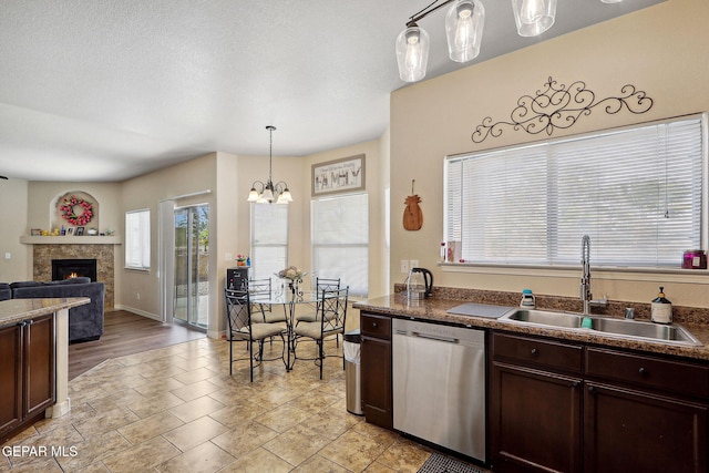 14309 Coyote Trl, El Paso, TX 79938 - kitchen with stainless steel dishwasher, a sink, a fireplace, dark brown cabinets, and a chandelier