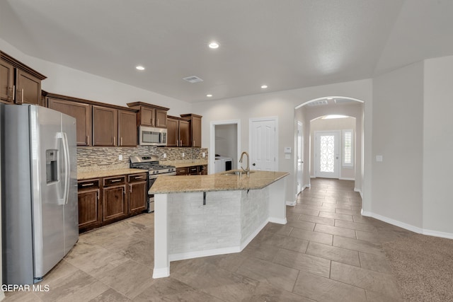 12776 Runway Ave, El Paso, TX 79928 - kitchen featuring appliances with stainless steel finishes, arched walkways, a sink, decorative backsplash, and light stone counters