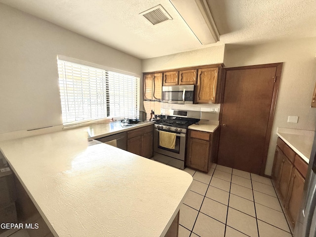 3224 Seabrook St, El Paso, TX 79936 - kitchen featuring appliances with stainless steel finishes, light countertops, a peninsula, brown cabinets, and a textured ceiling