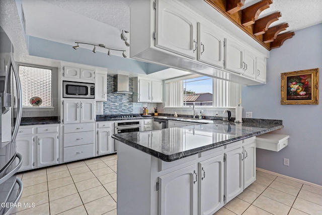 1428 Camino Alto Rd, El Paso, TX 79902 - kitchen featuring a peninsula, appliances with stainless steel finishes, wall chimney exhaust hood, light tile patterned flooring, and white cabinets
