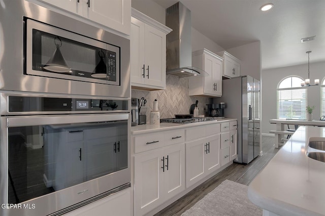 289 Hunstanton St, Horizon City, TX 79928 - kitchen with wall chimney exhaust hood, appliances with stainless steel finishes, wood finished floors, decorative backsplash, and white cabinets