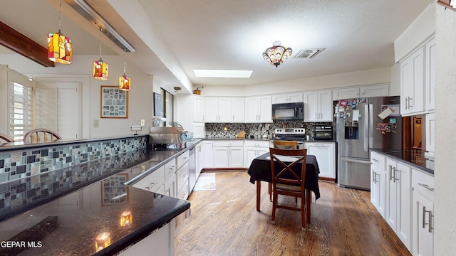 492 Country Oaks Dr, El Paso, TX 79932 - kitchen featuring appliances with stainless steel finishes, decorative backsplash, wood finished floors, white cabinetry, and a skylight