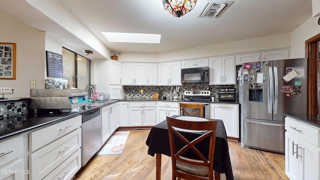 492 Country Oaks Dr, El Paso, TX 79932 - kitchen featuring appliances with stainless steel finishes, tasteful backsplash, a skylight, white cabinetry, and light wood-type flooring