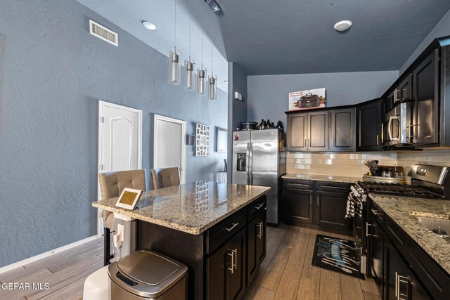 12805 Epsom Dr, Horizon City, TX 79928 - kitchen featuring appliances with stainless steel finishes, a textured wall, wood finished floors, light stone counters, and decorative backsplash