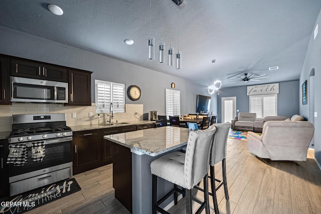 12805 Epsom Dr, Horizon City, TX 79928 - kitchen featuring appliances with stainless steel finishes, a sink, a kitchen breakfast bar, light stone counters, and light wood-type flooring