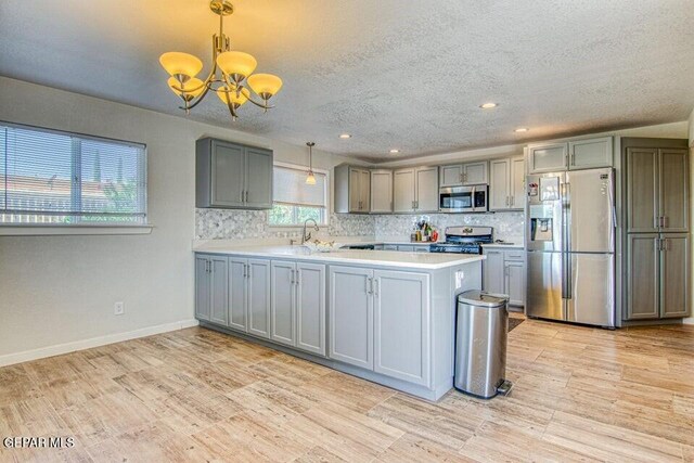 6504 Camino Fuente Dr, El Paso, TX 79912 - kitchen with stainless steel appliances, a chandelier, light countertops, light wood-type flooring, and a peninsula