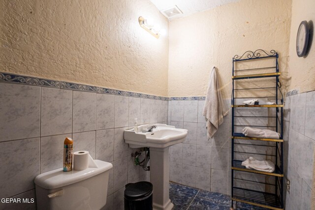 363 Ontiveros St, El Paso, TX 79932 - half bathroom with tile walls, toilet, wainscoting, a sink, and a textured wall
