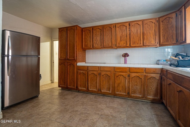 363 Ontiveros St, El Paso, TX 79932 - kitchen with freestanding refrigerator, brown cabinetry, and tasteful backsplash