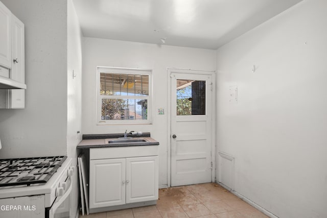1611 N Kansas St, El Paso, TX 79902 - kitchen with a sink, white cabinetry, under cabinet range hood, white gas range, and light tile patterned flooring