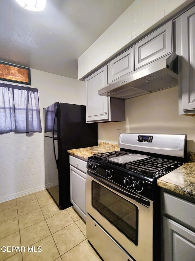 10077 Kirwood St, El Paso, TX 79924 - kitchen featuring gas range, under cabinet range hood, freestanding refrigerator, light tile patterned floors, and gray cabinets