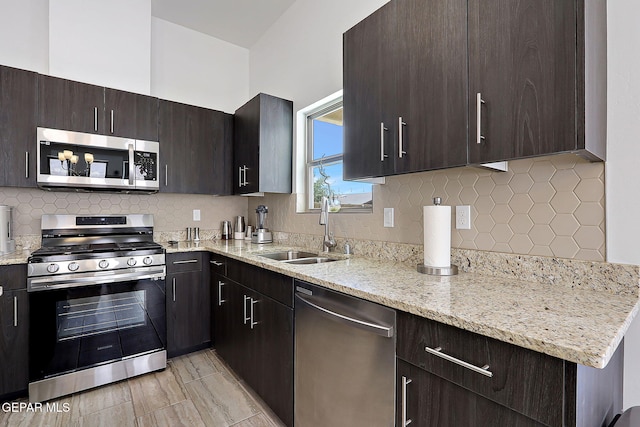 533 Cedarwood Ave, El Paso, TX 79928 - kitchen featuring appliances with stainless steel finishes, a sink, dark brown cabinetry, decorative backsplash, and light stone countertops