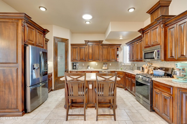 7301 Brays Landing Dr, El Paso, TX 79911 - kitchen featuring appliances with stainless steel finishes, backsplash, light stone counters, brown cabinetry, and a center island