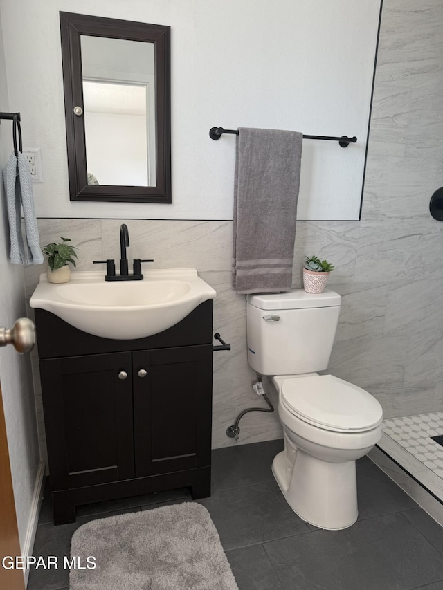 6220 Bel Mar Ave, El Paso, TX 79912 - bathroom featuring vanity, toilet, a tile shower, tile patterned floors, and tile walls