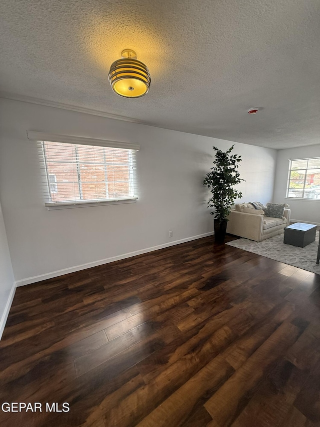 6220 Bel Mar Ave, El Paso, TX 79912 - unfurnished living room featuring a textured ceiling, dark wood-style floors, and baseboards