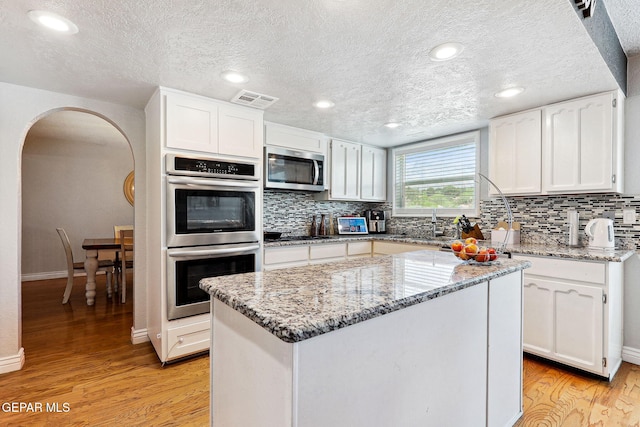 6008 Camino Alegre Dr, El Paso, TX 79912 - kitchen with appliances with stainless steel finishes, arched walkways, light wood finished floors, backsplash, and white cabinets