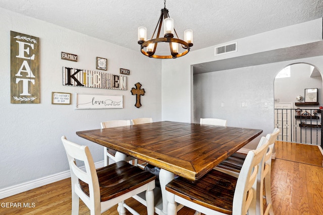 6008 Camino Alegre Dr, El Paso, TX 79912 - dining area featuring a chandelier, arched walkways, light wood-type flooring, a textured ceiling, and baseboards