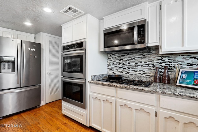 6008 Camino Alegre Dr, El Paso, TX 79912 - kitchen featuring appliances with stainless steel finishes, a textured ceiling, backsplash, white cabinets, and wood finished floors