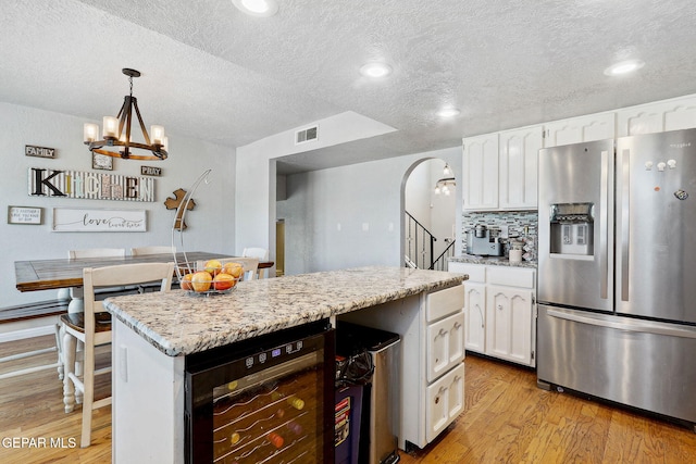 6008 Camino Alegre Dr, El Paso, TX 79912 - kitchen with stainless steel fridge with ice dispenser, wine cooler, light wood-style floors, white cabinetry, and a textured ceiling