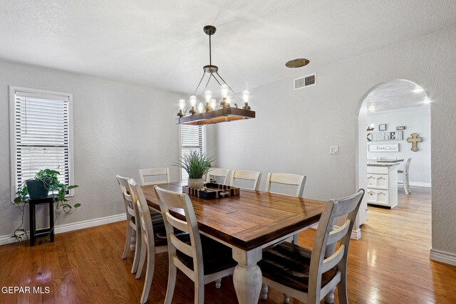 6008 Camino Alegre Dr, El Paso, TX 79912 - dining space featuring arched walkways, light wood-type flooring, baseboards, a textured wall, and a chandelier