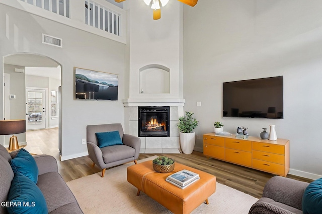 5965 Katelyn Gray Cir, El Paso, TX 79924 - living room with wood finished floors, a towering ceiling, arched walkways, a ceiling fan, and a tiled fireplace