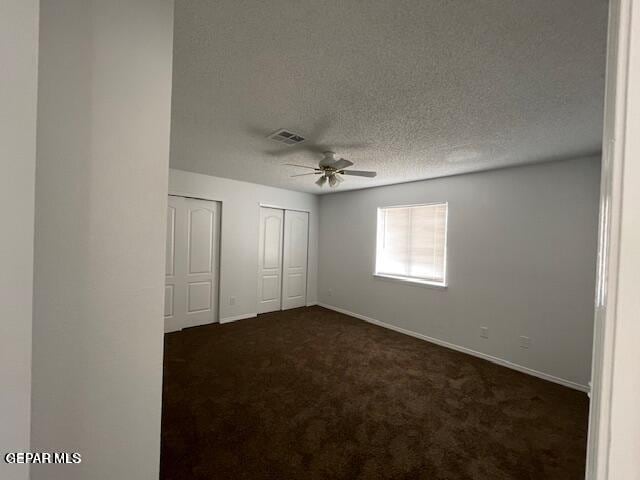 12501 Sombra Fuerte Dr, El Paso, TX 79938 - unfurnished bedroom featuring dark carpet, baseboards, two closets, a textured ceiling, and ceiling fan