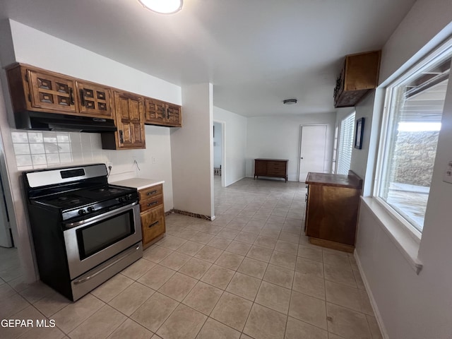 318 Olivia Cir, El Paso, TX 79912 - kitchen featuring gas range, under cabinet range hood, light tile patterned floors, backsplash, and baseboards