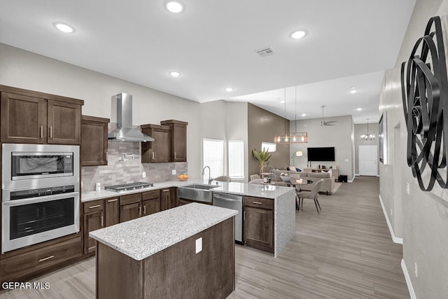 3936 Aspiration, El Paso, TX 79938 - kitchen featuring wall chimney range hood, appliances with stainless steel finishes, a sink, a peninsula, and a center island