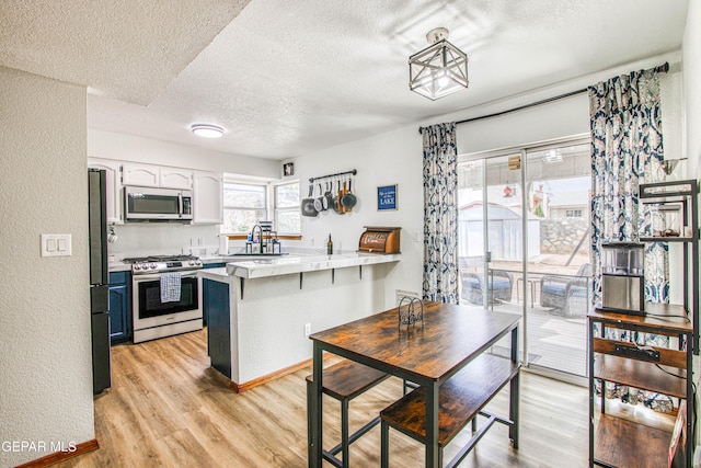 4521 Loma De Plata Dr, El Paso, TX 79934 - kitchen featuring appliances with stainless steel finishes, a peninsula, a textured ceiling, light wood finished floors, and a sink