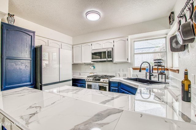 4521 Loma De Plata Dr, El Paso, TX 79934 - kitchen featuring appliances with stainless steel finishes, a textured ceiling, a sink, white cabinetry, and blue cabinets