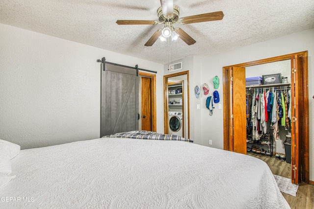 4521 Loma De Plata Dr, El Paso, TX 79934 - bedroom with washer / clothes dryer, wood finished floors, a textured ceiling, a barn door, and a walk in closet