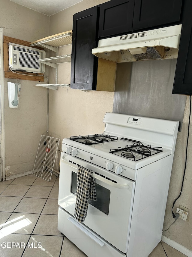 7800 Monterrey Dr, El Paso, TX 79915 - kitchen with white gas stove, under cabinet range hood, dark cabinetry, an AC wall unit, and light tile patterned floors